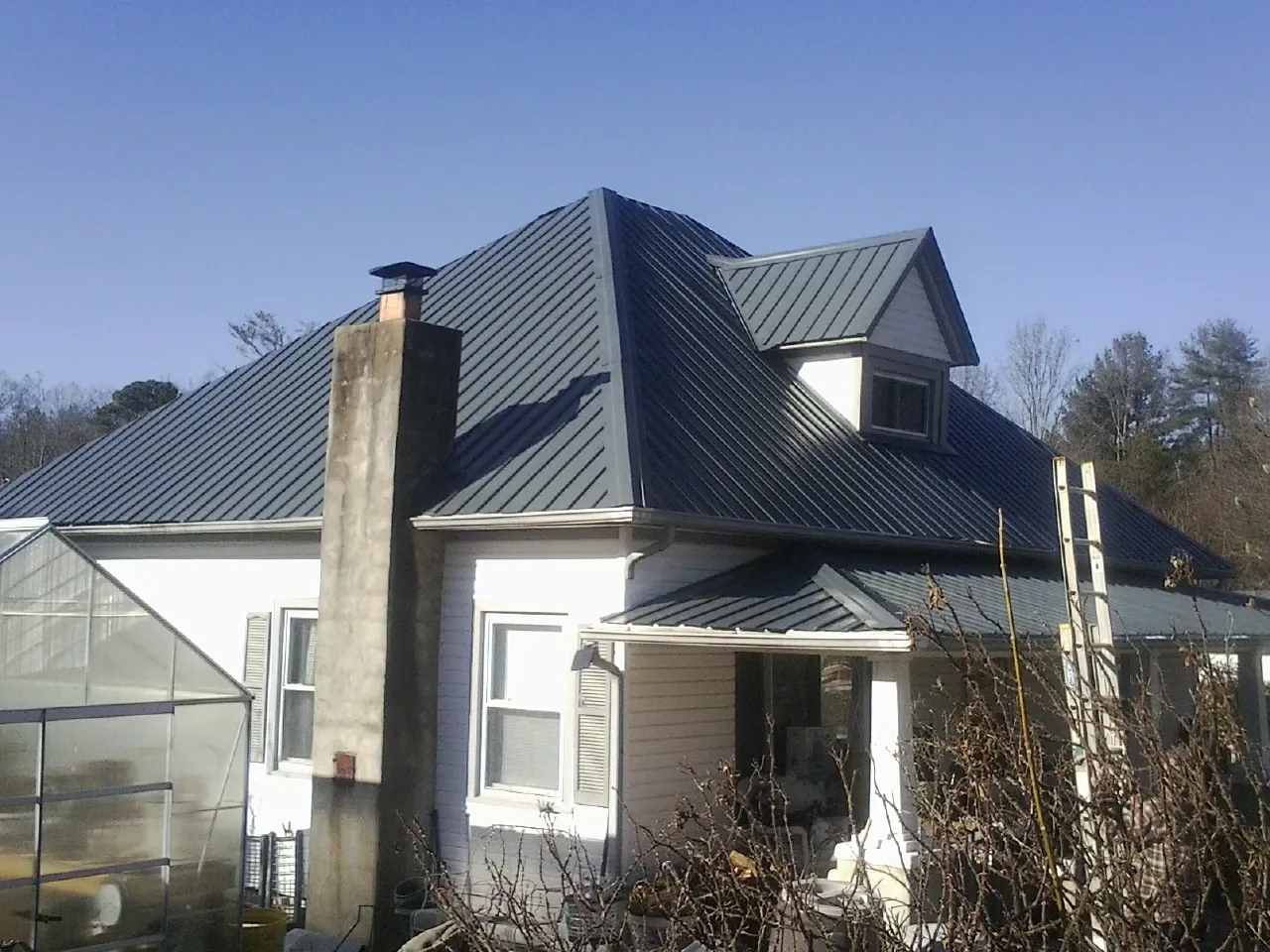 Dark blue standing seam metal roof on a white farmhouse with dormer — Slate & Tile Roof Repair by Roofing Brothers in Park Valley