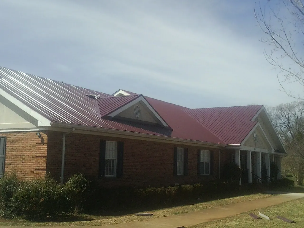 Red metal roof with gabled entries on a long brick building, from a Hail Damage Roof Repair job in Park Valley