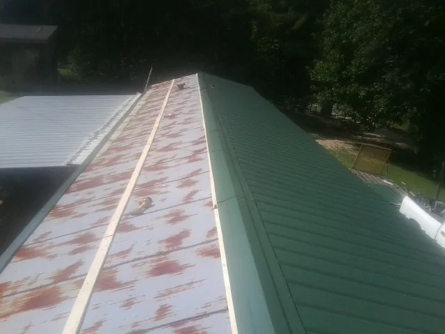 Old rusted panels beside newly installed green metal roofing — Wind Damage Roof Repair by Roofing Brothers in Park Valley