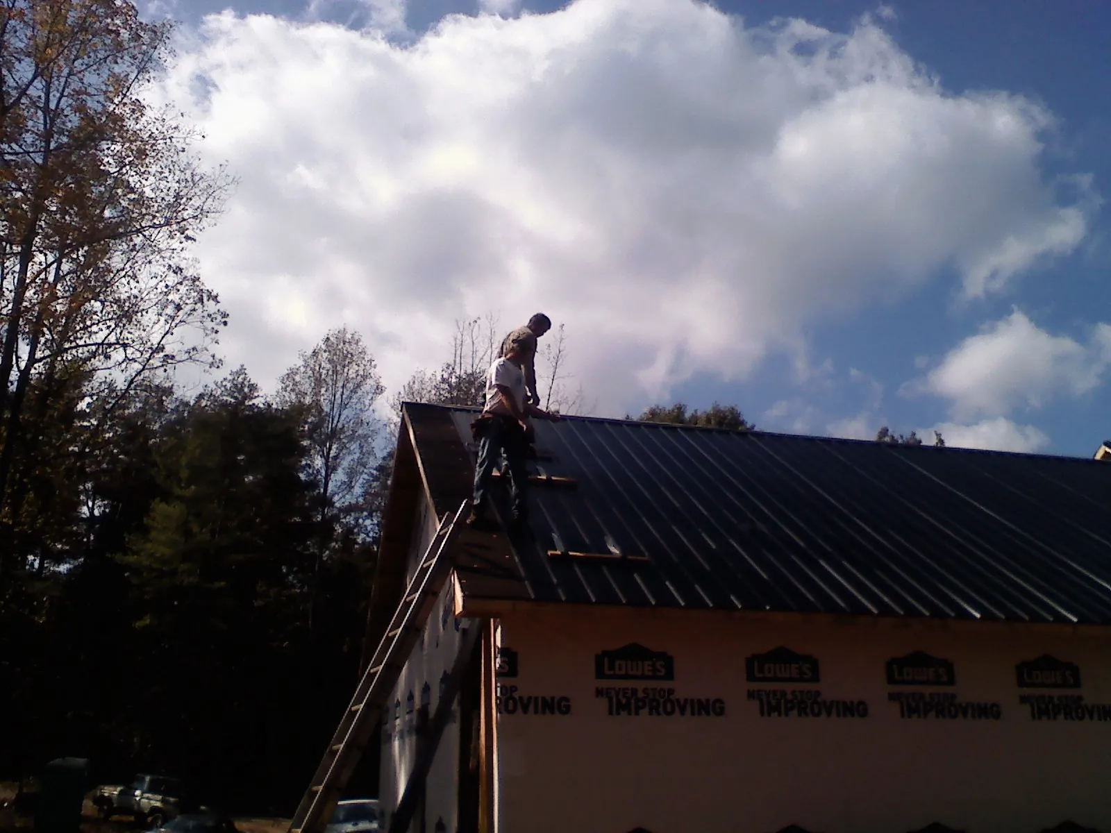 Roofer fastening dark metal panels high against a cloudy sky, from a Roof Inspection job in Park Valley