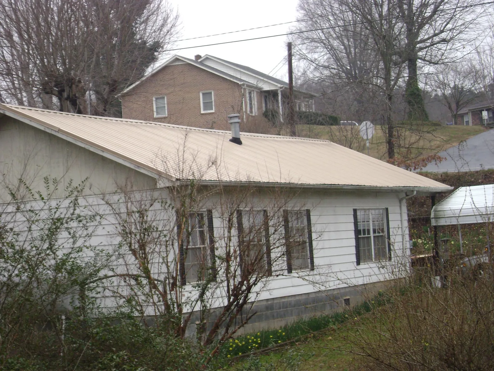 Tan metal roof on a white sided house set into a hillside — Commercial Roofing by Roofing Brothers in Park Valley
